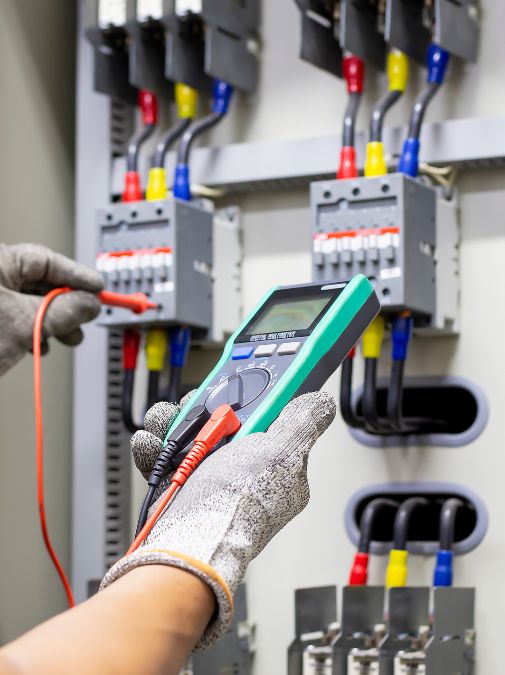 Technicien en gants utilisant un appareil de mesure électrique sur un tableau de contrôle